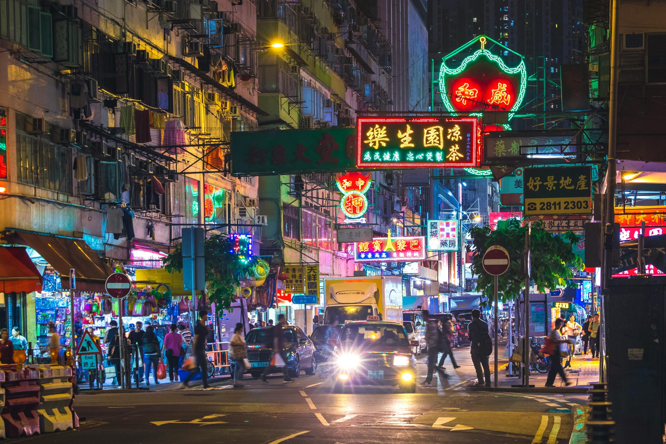 Colorful neon lights illuminate a bustling street in the New Territories, Hong Kong, by night.